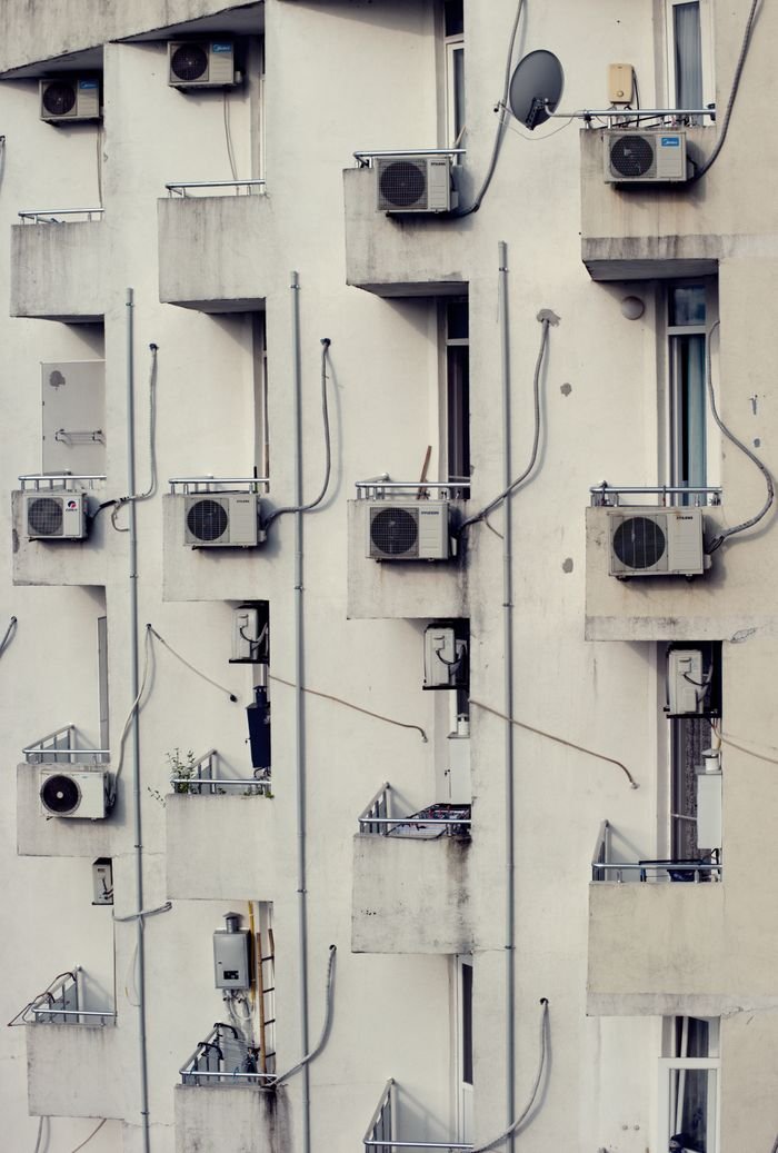 Vertical view of modern apartments with balconies featuring air conditioning units.