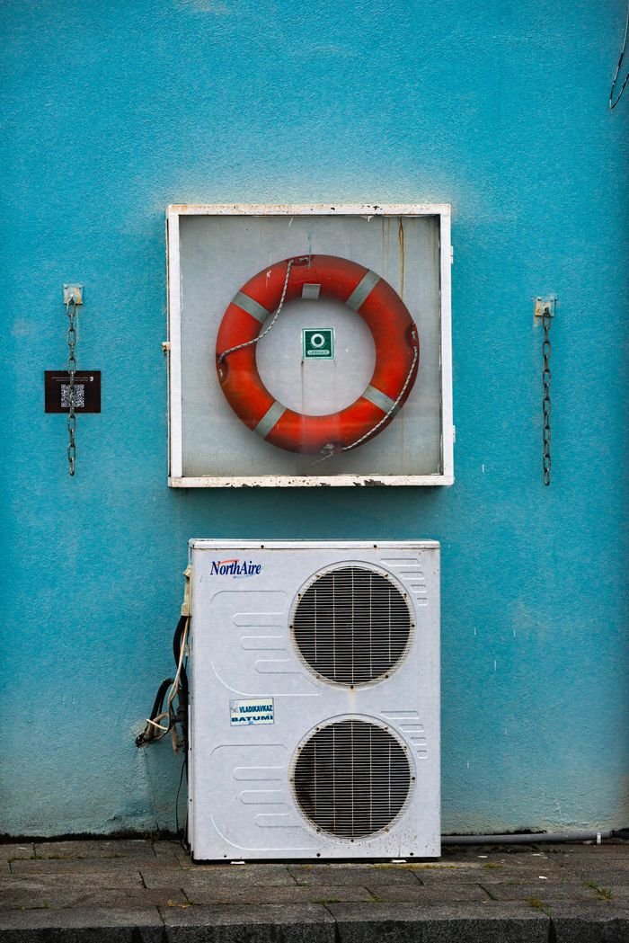 Outdoor wall with a lifebuoy and air conditioning unit on a bright blue background.